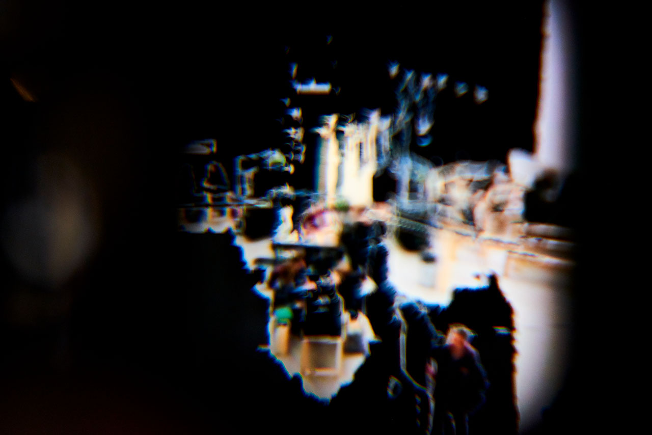 A photographed view through a VR headsets shows a gallery space with people and objects in dark colors. The colors smear as though some of the people and objects are in motion.