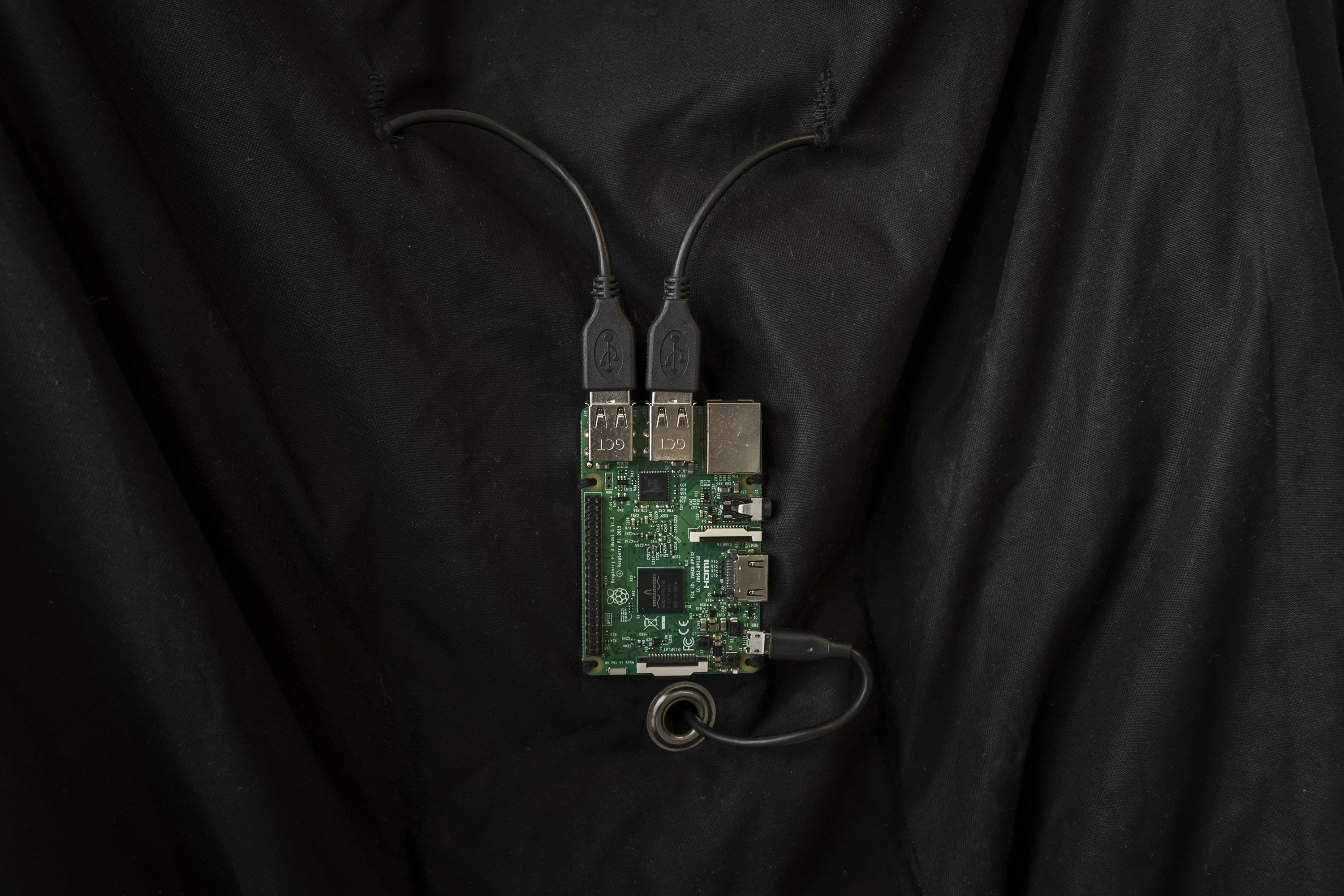 A Raspberry Pi computer is sewn onto the black fabric of a self-made VR suit. Three cables connect to the circuit board and disappear into the fabric.