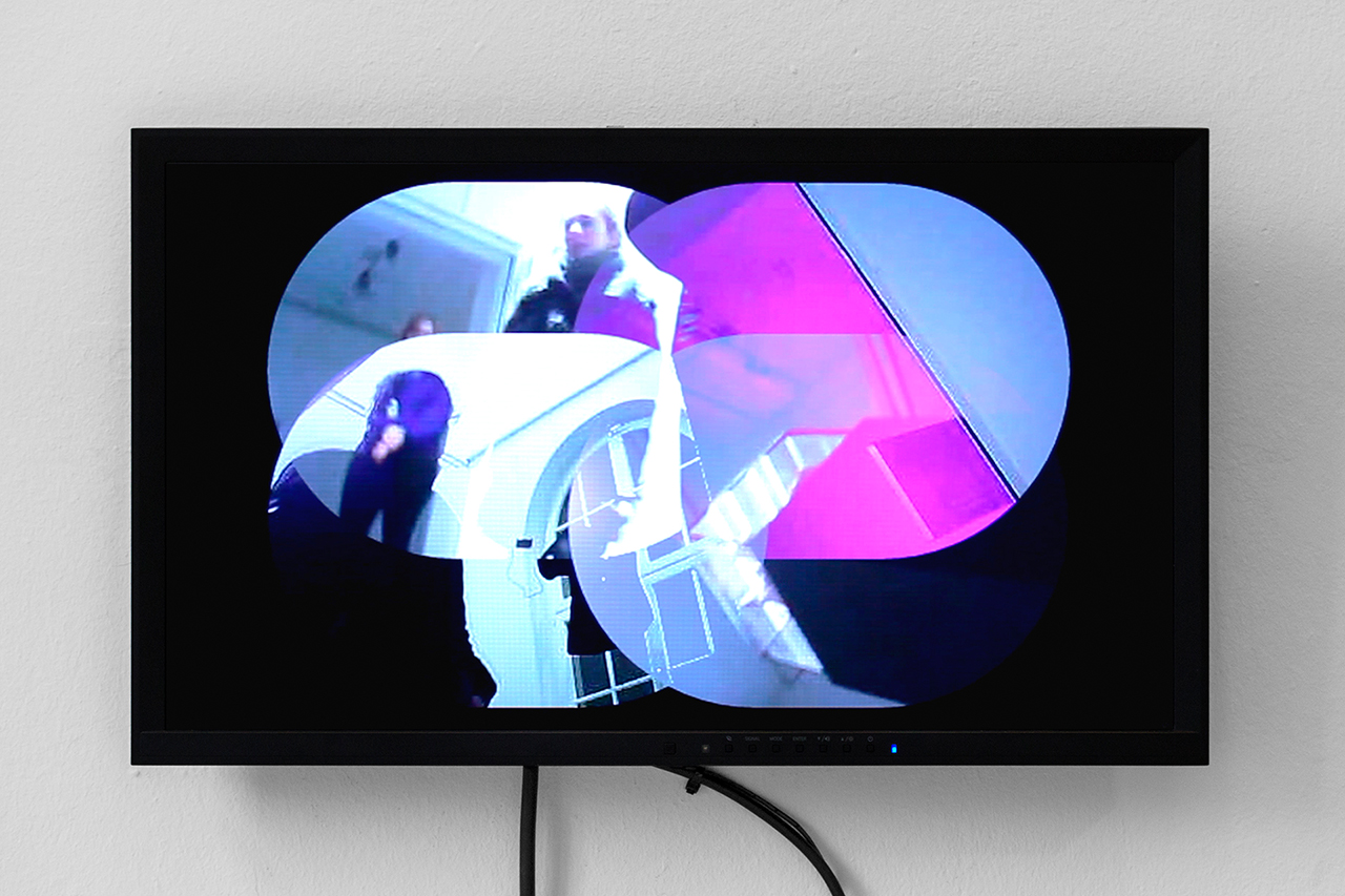 On a computer screen, four video images are arranged that overlap and merge into one another. Each video feed shows the input of another camera. People and a window with a VR suit hanging in front of it can be sen from four different perspectives.