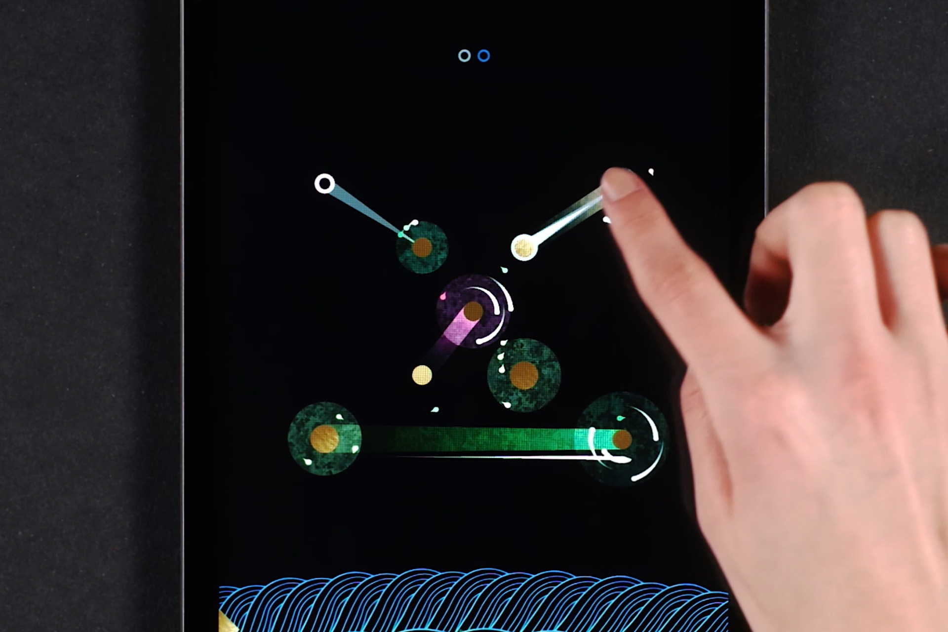 On an ipad, a puzzle of the game SHIRO is opened and shows moons with colorful circles around them. A white person's hand reaches into the frame and connects two of the moons, thereby making little droplets move between them.