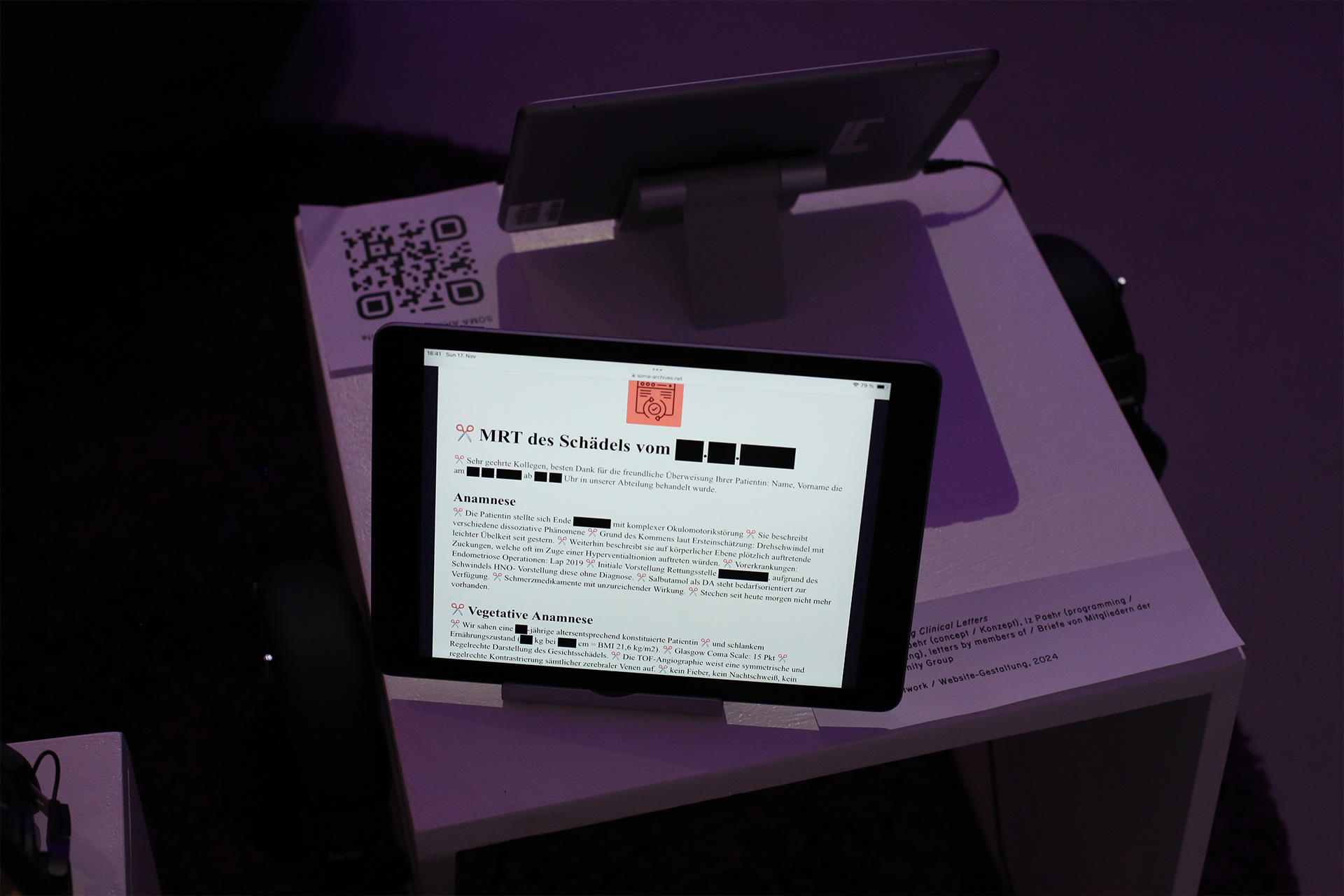 A website artwork is presented on a tablet in an exhibition space with violet lighting. The website features a clinical letter titled 'MRT of the head at' with the date blocked out. This letter is generated from multiple letters, and each new part is indicated by a scissor icon.